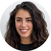 Ambra, ritratto in primo piano: donna sorridente con lunghi capelli scuri ricci e maglia nera, su fondo chiaro