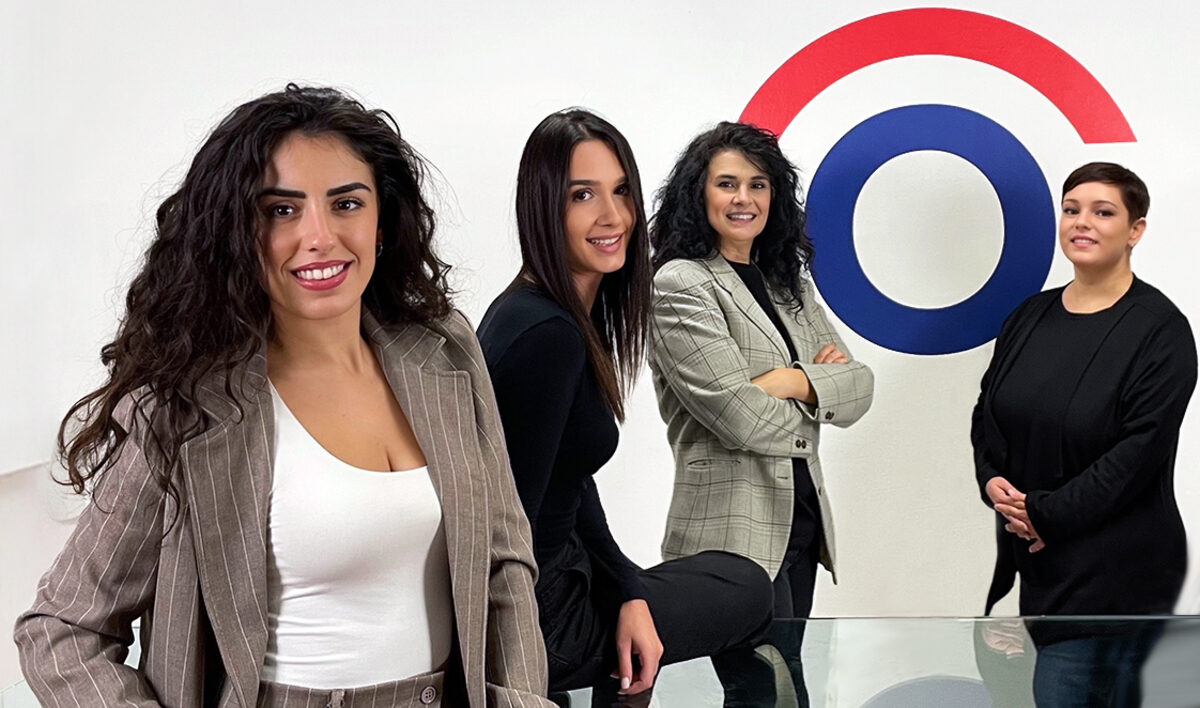 Quattro donne dello staff direttivo di OmnitekStore, in ufficio davanti alla parete con il logo dell'azienda